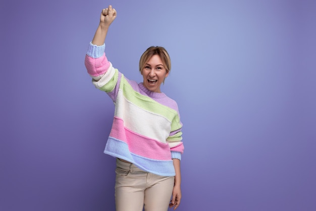 Successful charming blond young woman raised her hand into a fist on a purple background