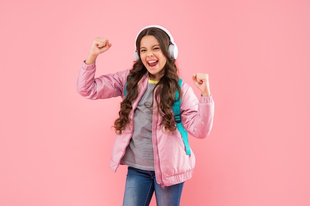 Successful child listen music in headphones and carry backpack on pink background music