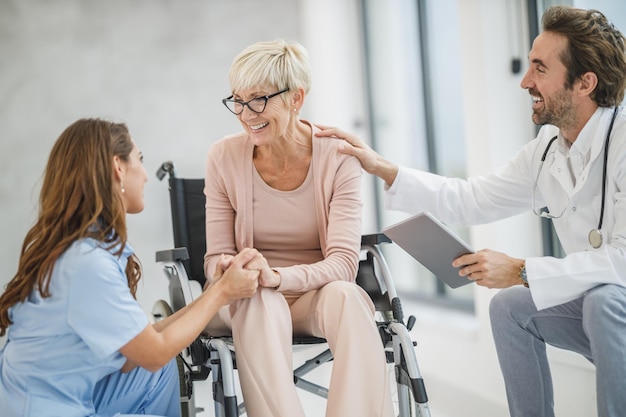 Successful doctor and young nurse talking with their senior female wheelchair-bound patient.