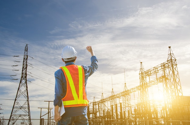 Successful engineer standing at the power substation against the sunrise background