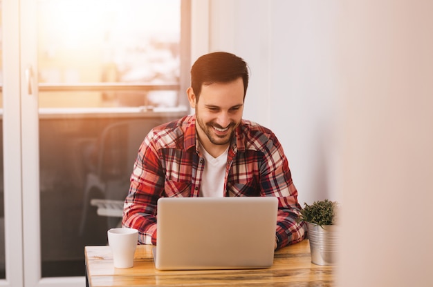 Successful entrepreneur smiling in satisfaction as he checks information on his laptop computer while working in a home office. Lens flare