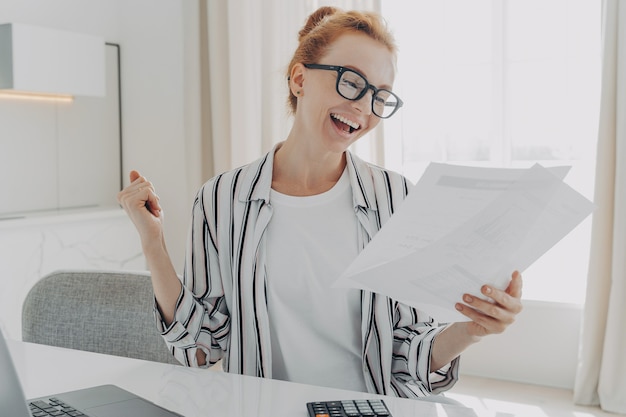 Successful female manager plans budget checks finances makes fist pump holds paper documents