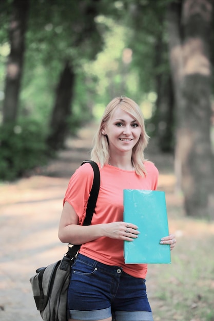 Successful female student with a bag and a clipboard on the background of the Park