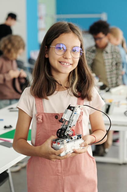 Successful girl in casualwear and eyeglasses holding robot constructed at lesson