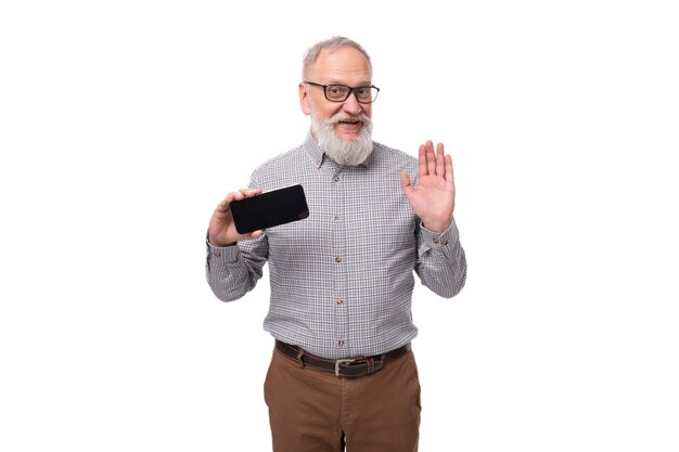 Successful grandfather with a gray beard and mustache in glasses shows a phone screen with a mockup