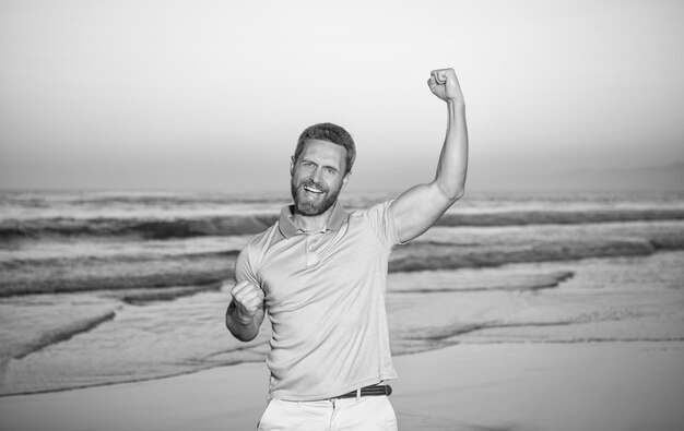 Photo successful guy on sunrise beach bearded man in shirt celebrate success summer vacation