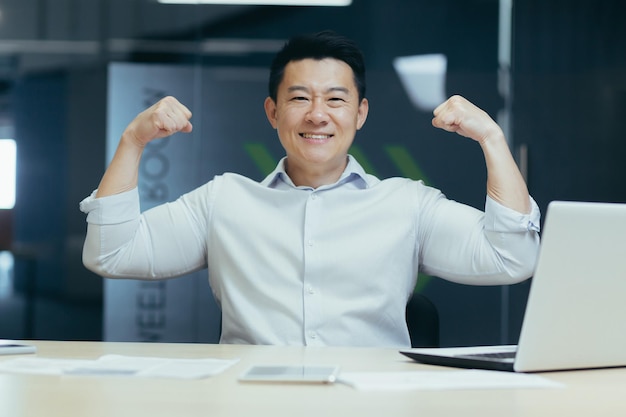 A successful and handsome young asian business man looks at the camera smiles shows with his hands