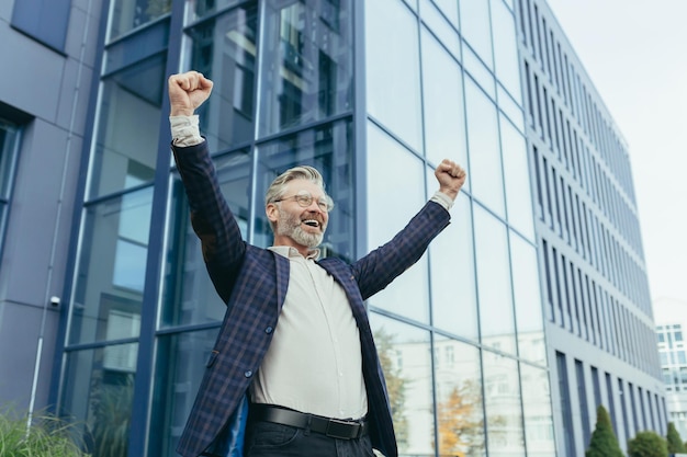 Successful and happy grayhaired boss outside office building rejoices success and victory triumphs