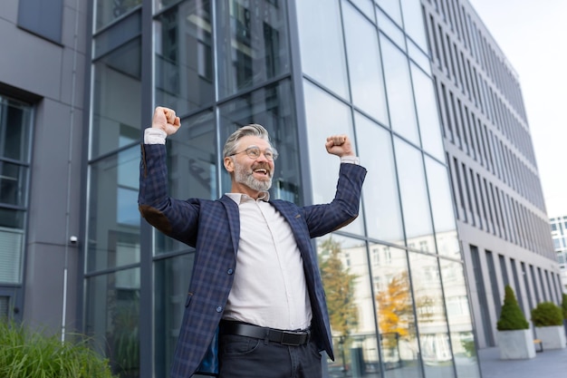 Successful and happy grayhaired boss outside office building rejoices success and victory triumphs