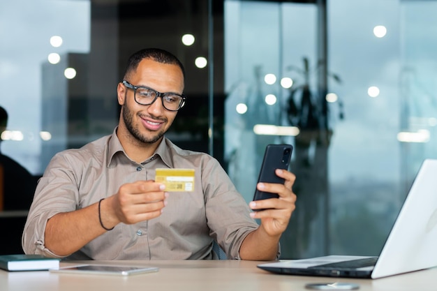 Successful hispanic businessman inside office man in shirt smiling and happy holding bank credit