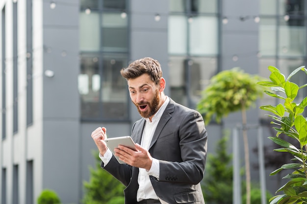 Successful male businessman got good win news reads them from a tablet computer, rejoices and thanks for the victory and success