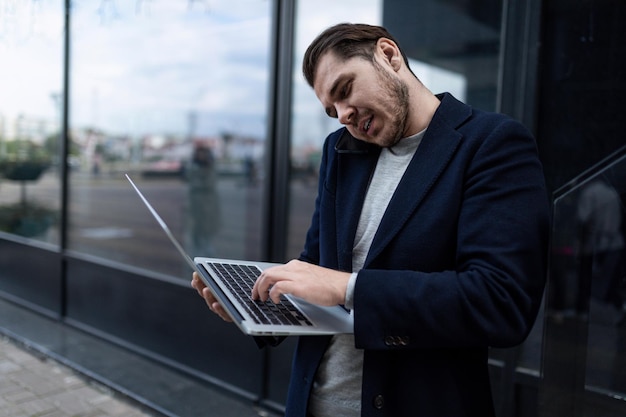 Successful male businessman speaks on the phone with his head pressed to his shoulder and typing on