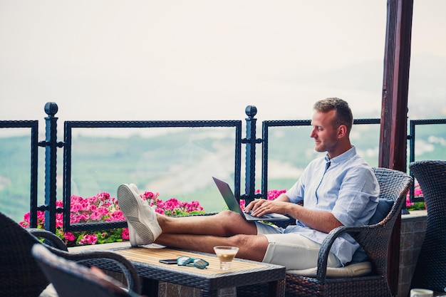 Successful male businessman working on vacation behind a laptop with a mountain view Online manager workflow Work outdoors with a beautiful view from the balcony