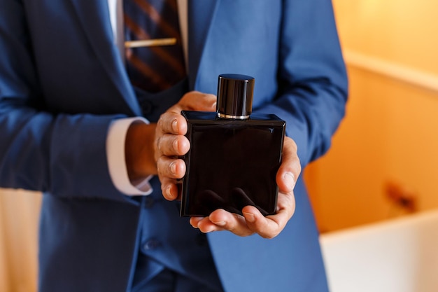 Successful man in blue formal suit holding on hands expensive black bottle of perfumes