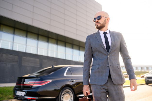 Successful man in a suit with a briefcase on the background of an expensive car