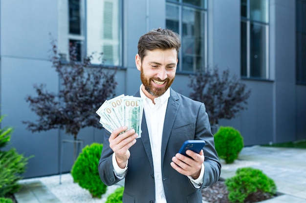 Successful man winner holds dollars in cash, rejoices in winning by phone, businessman rejoices