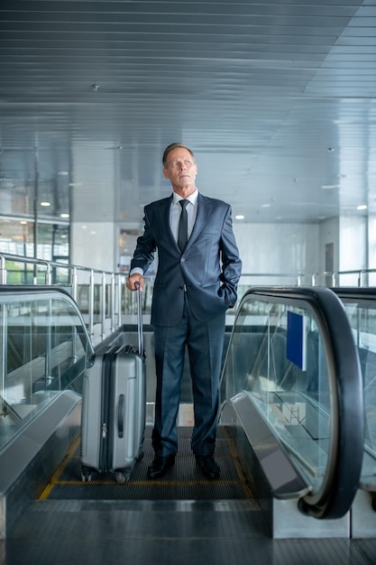 Successful man with suitcase going up on escalator