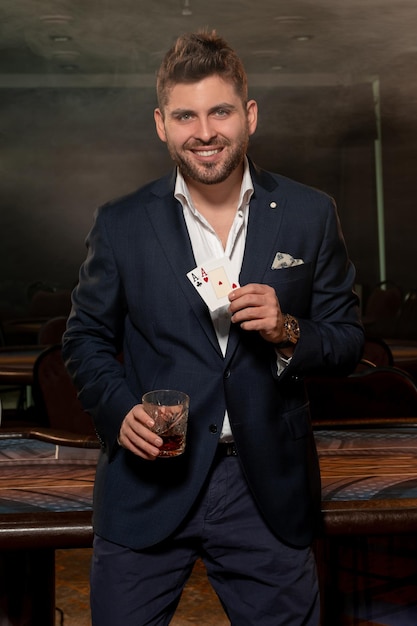 Successful man with two aces in hand celebrating poker win with glass of brandy