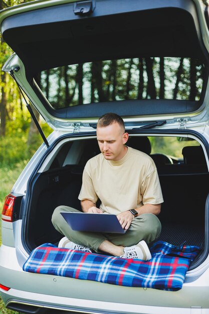 Successful man working outdoors from his car sitting in the trunk and looking at the laptop Online remote worker lifestyle concept Copy space