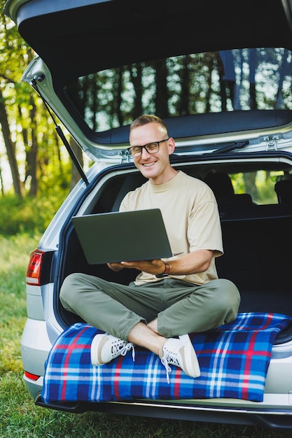 Successful man working outdoors from his car sitting in the trunk and looking at the laptop Online remote worker lifestyle concept Copy space