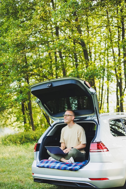 Successful man working outdoors from his car sitting in the trunk and looking at the laptop Online remote worker lifestyle concept Copy space