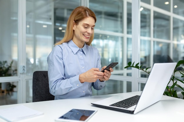 Photo successful mature businesswoman boss using phone at workplace inside modern bright office office