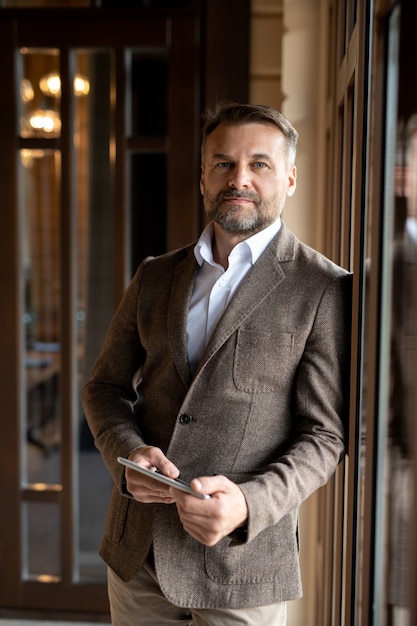 Successful mature elegant businessman with tablet looking at you while standing in front of camera