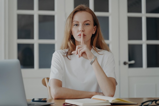 Successful mid adult businesswoman is working from home and gestures hush Concept of secret