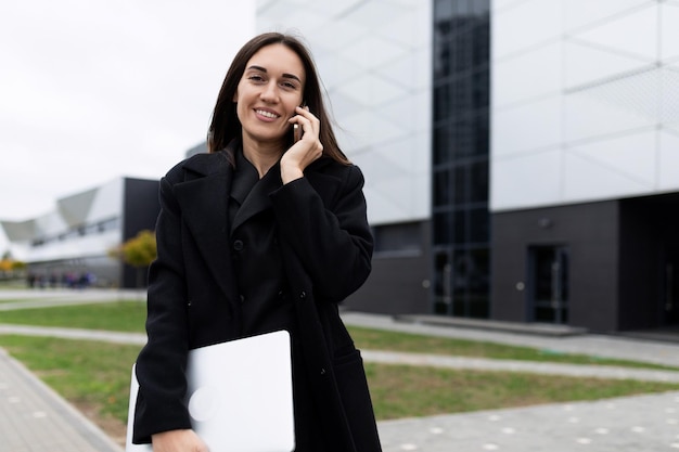 Successful modern caucasian woman talking on mobile phone with laptop on office background