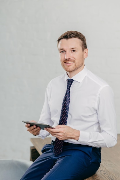 Successful owner of financial company wears elegant clothes reads notification or chatts with friends on modern touch pad has gentle smile looks confidently at camera People and technology concept