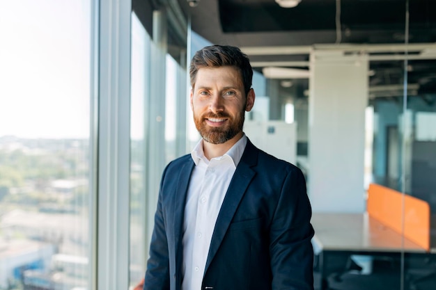 Successful person Handsome businessman in formal wear standing in office near window looking and smiling at camera