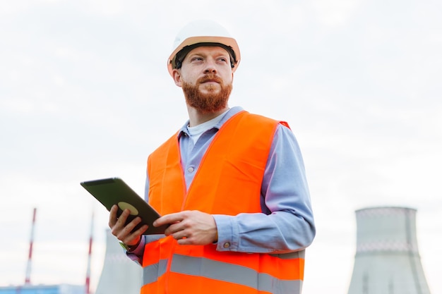 A successful professional The man is an engineer in a helmet and a protective orange vest Tablet in hand