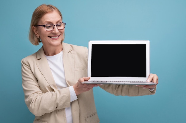 Successful s middle aged woman in jacket with laptop to work on studio background with copy space