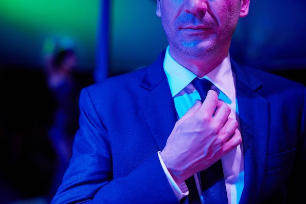 Successful yet seedy Shot of a seedy businessman adjusting his tie in a go go bar with a woman dancing on a pole behind him