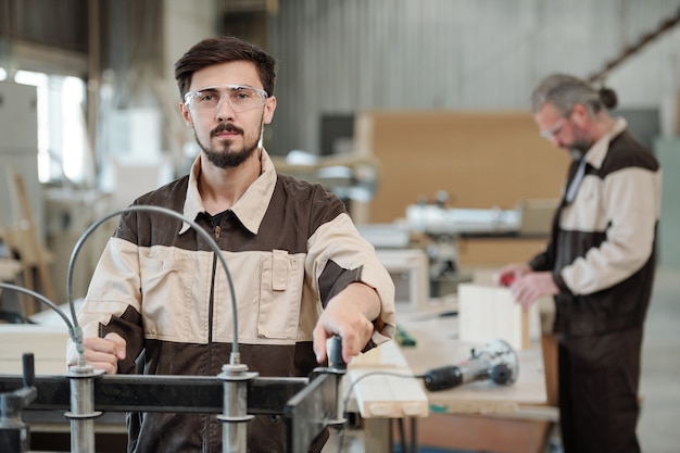 Successful senior master of contemporary furniture producing factory standing with partner behind