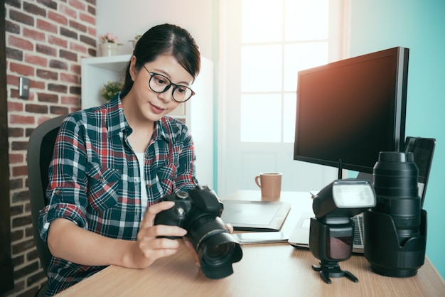 successful seriously female business photo making woman holding camera review working picture and sitting on office desk ready to transport for editing retouch.