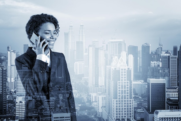 Successful smiling black African American business woman in suit pensively talking phone Kuala Lumpur cityscape The concept of consultants as problem solvers KL skyscrapers Double exposure