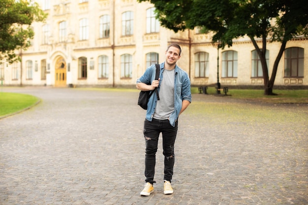 Successful student man is standing with backpack behind park near campus.