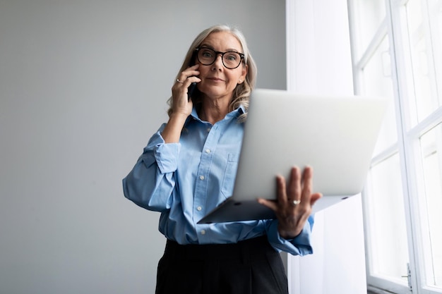 Successful woman manager with a laptop in her hands speaks on a mobile phone at the office window