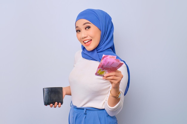 Successful young Asian Muslim woman holding wallet and money banknotes isolated over white background