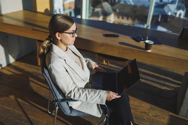 Successful young business woman in glasses with laptop in office Business woman sending email message and working on laptop Young business woman sitting at workplace