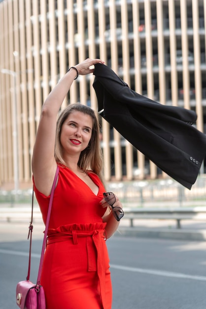 Successful young business woman in red dress swings jacket over her head Vertical frame