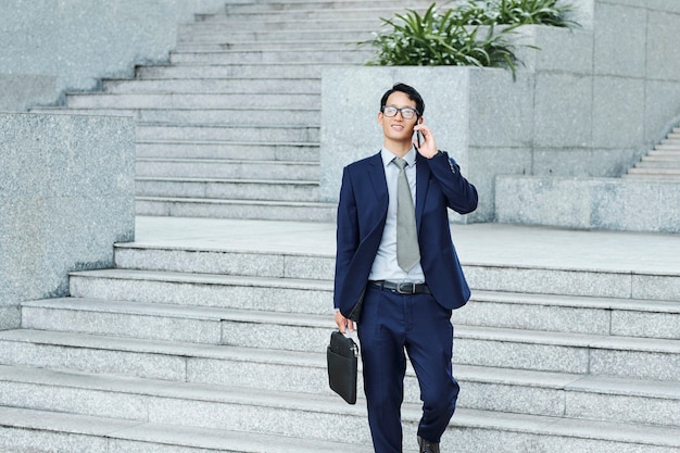 Successful young businessman with briefcase walking in the street and talking on phone