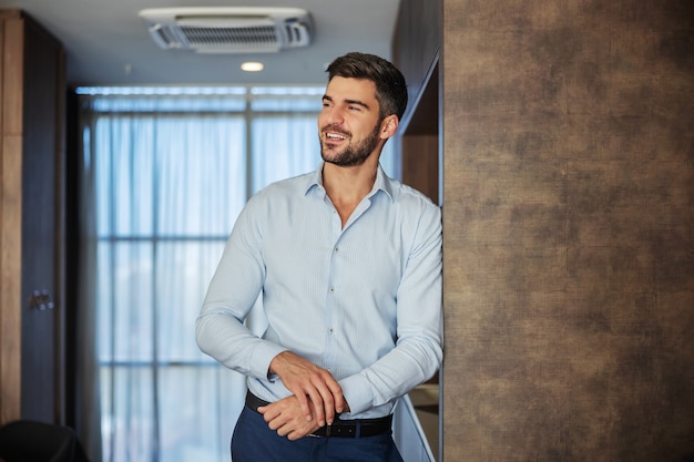 A successful young handsome man in a formal shirt and pants looks to the side with a smile