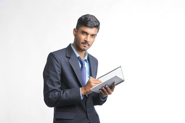 Successful Young Indian businessman or employee wearing Suit and cheaking dairy on white background.