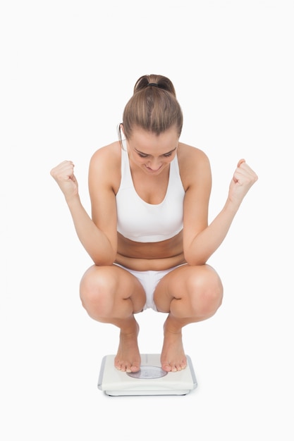 Photo successful young woman crouching on a scales