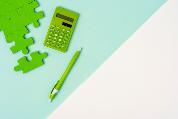 A successfully folding puzzle a green calculator and a ballpoint pen on a whiteturquoise background the concept of payments taxes purchases and financial actions