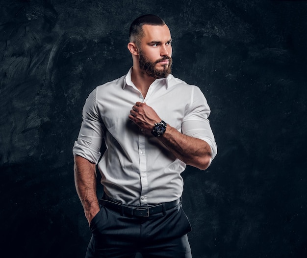 Sucessful bearded businessman in white shirt is posing at dark photo studio.