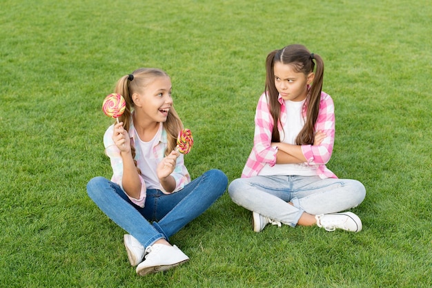 Sugar and calories Joyful cheerful friends eating sweets outdoors Candy shop Lollipop treats Candy means happiness Holiday food Confectionery Sweet caramel Happy children hold candy sit grass