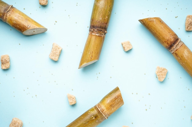 Sugar cane and brown sugar pieces on blue background Top view